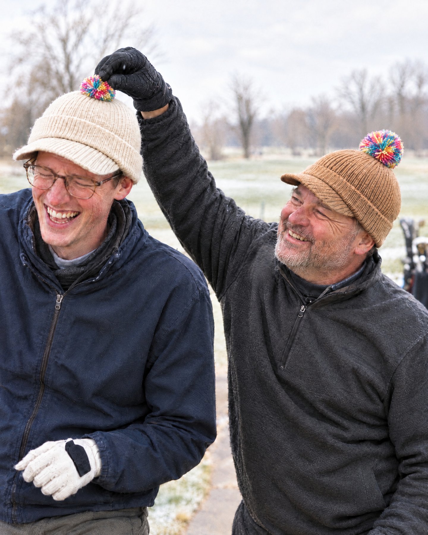 One golfer laughs as his friend tugs the pom on his Cream bobbn beanie, both wearing Camel and Cream